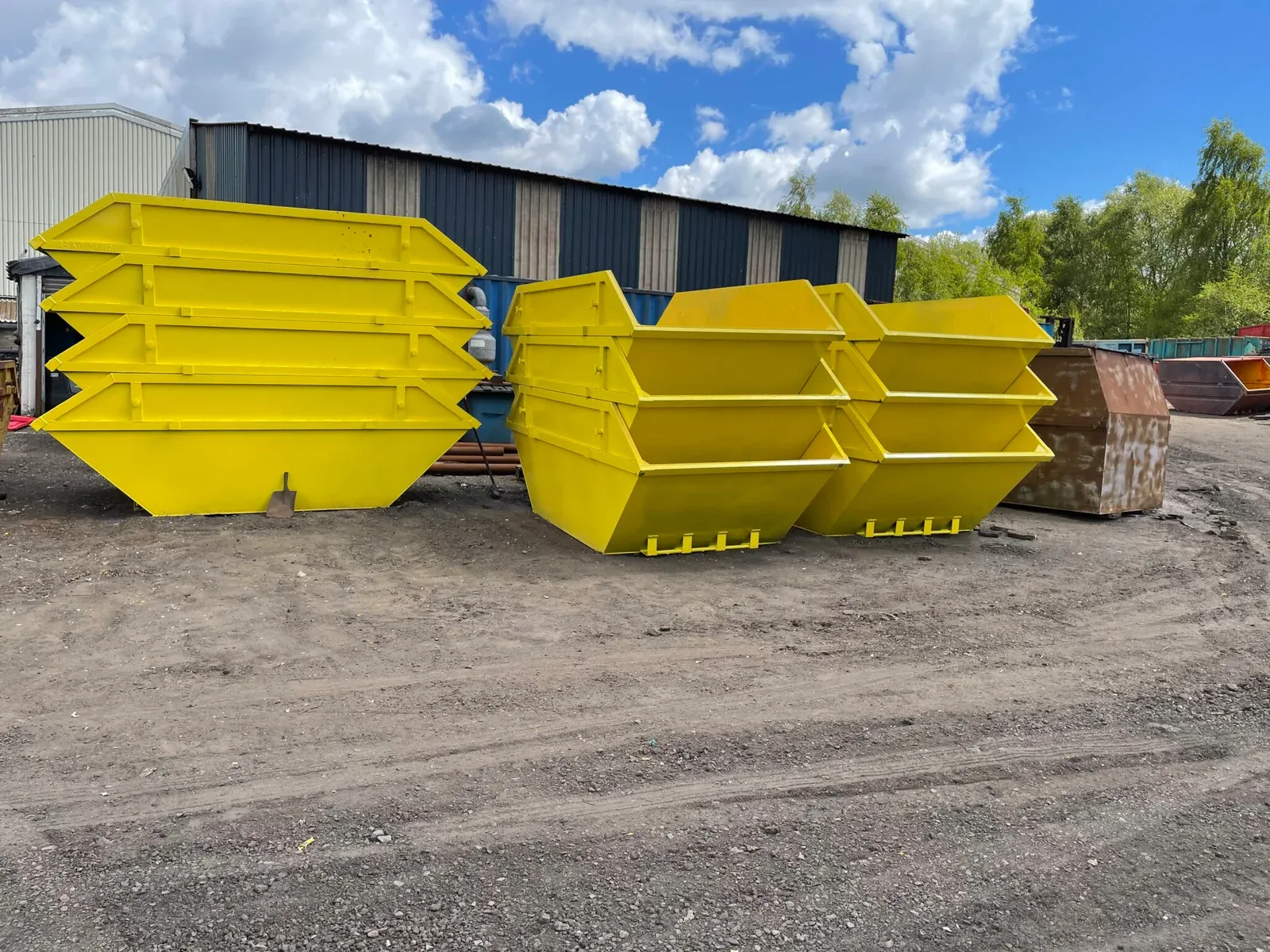 Newly built skips, painted yellow and stacked in the yard ready for delivery